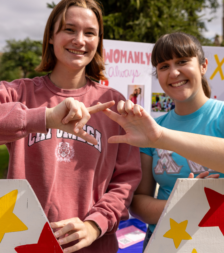 two students making sorority sign in the quad