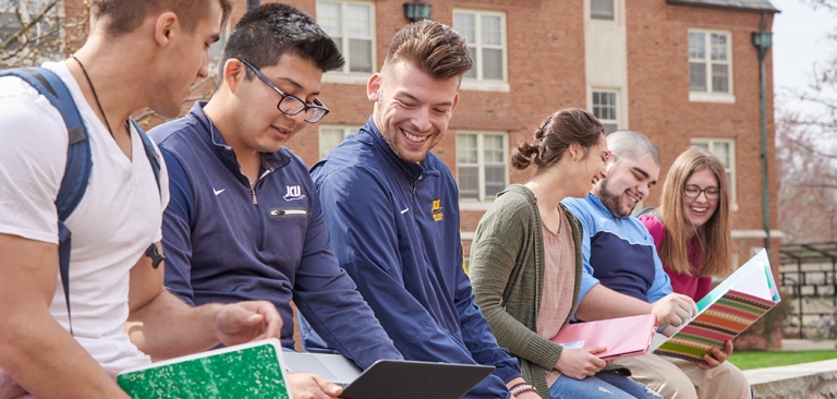 Group of students sitting on brick ledge reading books